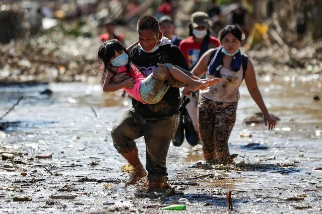 A man carries a girl through debris and floods in the typhoon-damaged Kasiglahan village in Rodriguez, Rizal province, Philippines on Friday, November 13, 2020. Thick mud and debris coated many villages around the Philippine capital Friday after Typhoon Vamco caused extensive flooding that sent residents fleeing to their roofs and killing dozens of people. (Photo by Aaron Favila/AP Photo)