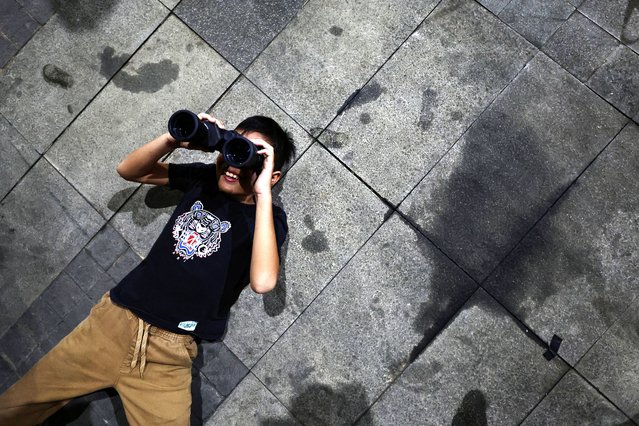 A boy uses binoculars to observe the 'Blood Moon' during a total lunar eclipse in Jakarta, Indonesia, on September 7, 2025. (Photo by Willy Kurniawan/Reuters)