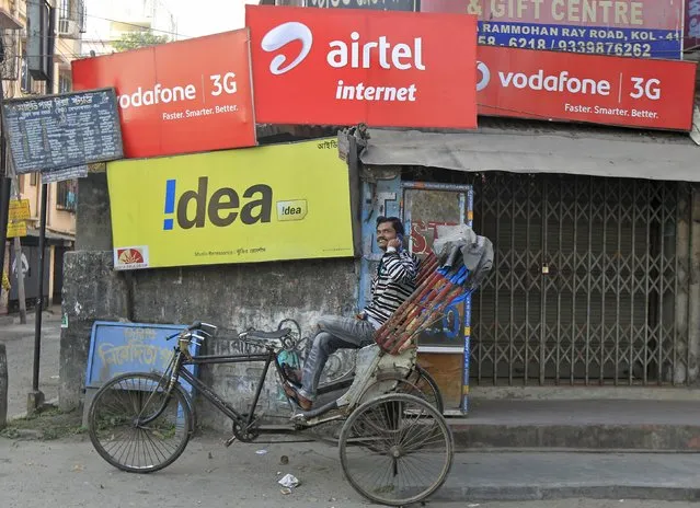 A rickshaw puller speaks on his mobile phone as he waits for customers in front of advertisement billboards belonging to telecom companies in Kolkata in this February 3, 2014 file photo. (Photo by Rupak De Chowdhuri/Reuters)