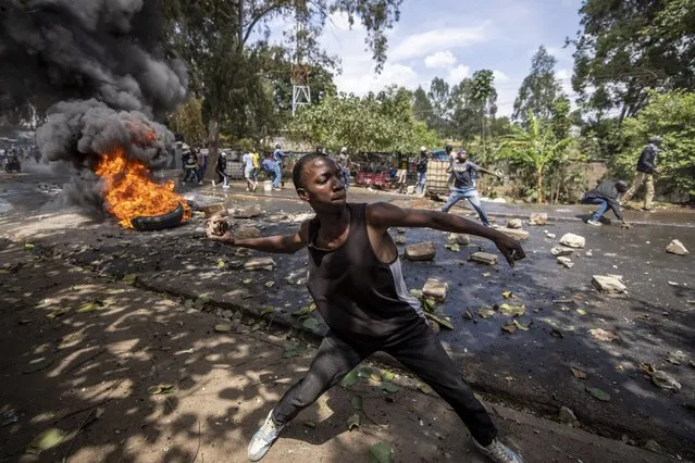 A protester throws rocks towards police in the Kibera slum of Nairobi, Kenya, Monday, March 20, 2023. Hundreds of opposition supporters have taken to the streets of the Kenyan capital over the result of the last election and the rising cost of living, in protests organized by the opposition demanding that the president resigns from office. (Photo by Ben Curtis/AP Photo)