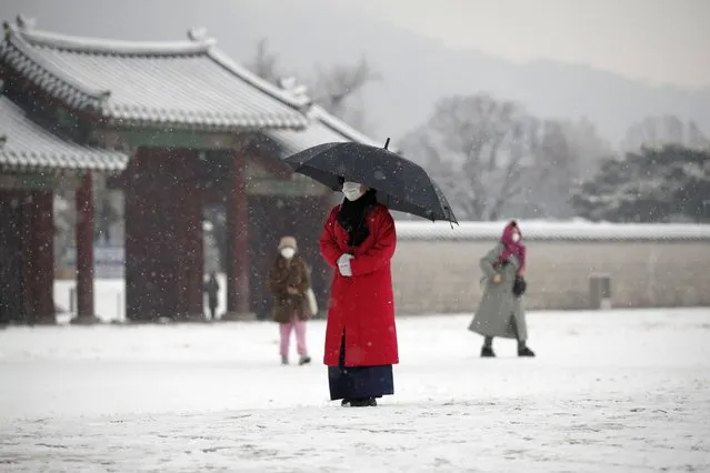 An employee wearing a face mask as a precaution against the coronavirus uses an umbrella to take shelter from the snow at the Gyeongbok Palace, one of South Korea's well-known landmarks, in Seoul, South Korea, Sunday, December 13, 2020. (Photo by Lee Jin-man/AP Photo)