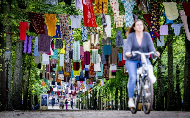 A woman rides her bicycle below dresses donated by survivors of sexual violence that hang from clotheslines spanned across the Lange Voorhout, in The Hague, Netherlands, 19 June 2024. With the art installation titled “Thinking of You” its creator, artist Alketa Xhafa Mripa, intends to draw attention to people who have experienced sexual violence in conflict situations. (Photo by Robin Utrecht/EPA)