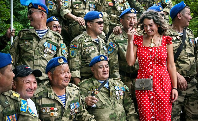 A woman poses for a photo with Kyrgyzstan's veterans next to a monument to Soviet soldiers killed in action in Afghanistan during Soviet invasion of 1979-1989, marking the annual Combat Veterans Day at Poklonnaya Hill War Memorial Park in Moscow on July 1, 2024. (Photo by Alexander Nemenov/AFP Photo)