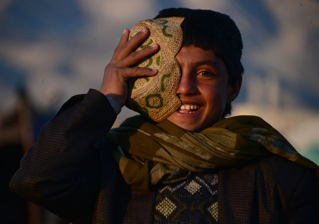 An Afghan child adjusts his hat as he stands near his tent on the outskirts of Herat on November 26, 2015. (Photo by Aref Karimi/AFP Photo)