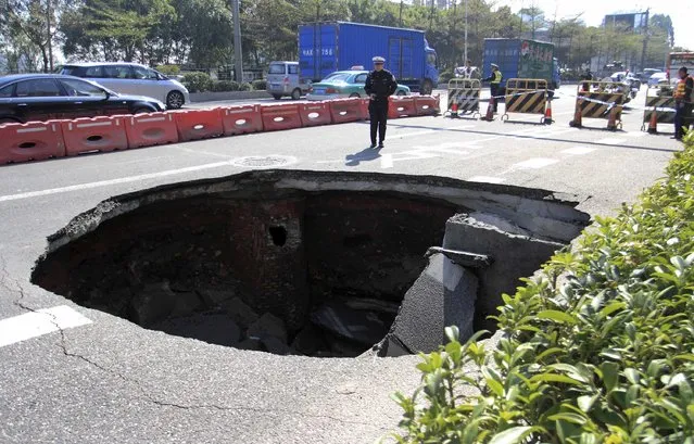 A policeman stands next to a caved-in area on a street in Guangzhou, Guangdong province, January 14, 2015.  A car was stranded when the cave-in, measuring approximately 25-square-metres, occurred on Wednesday morning. No one was injured, according to local media. (Photo by Reuters/Stringer)