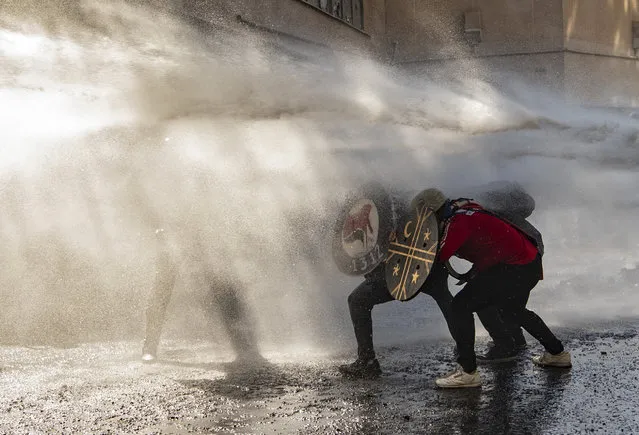 Demonstrators use shields to protect themselves from water sprayed by riot police during clashes on the commemoration of the first anniversary of the social uprising in Chile, in Santiago, on October 18, 2020, as the country prepares for a landmark referendum. Changing the constitution enacted under former dictator Augusto Pinochet, who ruled from 1973-90, was a key demand of protesters during the two months of violent civil unrest against the government and inequality. Chileans will be asked two questions on October 25: do they want a new constitution and who should draft it. (Photo by Martin Bernetti/AFP Photo)