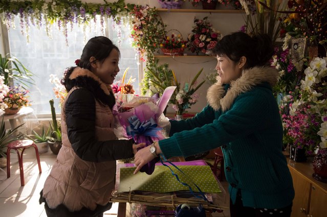 In a photo taken on November 16, 2016 a woman buys flowers from a vendor in Pyongyang. The North Korean capital was celebrating “Mother's Day”, a public holiday reportedly started in 2012 with the aim of “honouring all mothers” including the ruling Workers Party, often referred to as the “Mother Party”. (Photo by Kim Won-Jin/AFP Photo)
