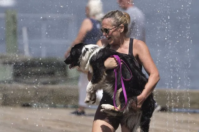 A woman carries her dog through a water fountain on the Halifax waterfront in Halifax, Nova Scotia, Thursday, July 6, 2023. (Photo by Darren Calabrese/The Canadian Press via AP Photo)