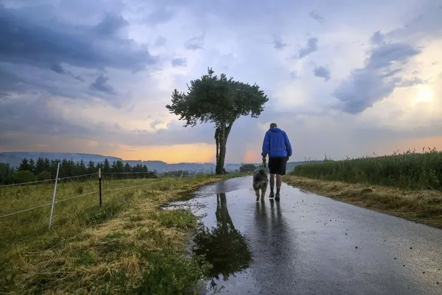 A man walks his dog in the morning shortly after sunrise, while thunderclouds gather in the background, in Riedlingen, Germany, Wednesday, June 21, 2023. Authorities in Germany warned Wednesday that the country could experience severe storms with significant amounts of rainfall in the coming days. (Photo by Thomas Warnack/dpa via AP Photo)