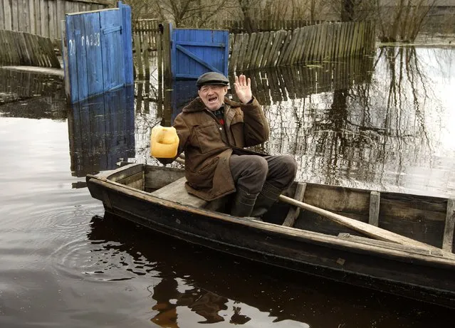 A man gestures on a boat along a flooded street as water from the Prypyat river overflows its banks during spring flooding in the village of Khlupin, some 270 km (168 miles) south of Minsk, April 15, 2013. (Photo by Vasily Fedosenko/Reuters)