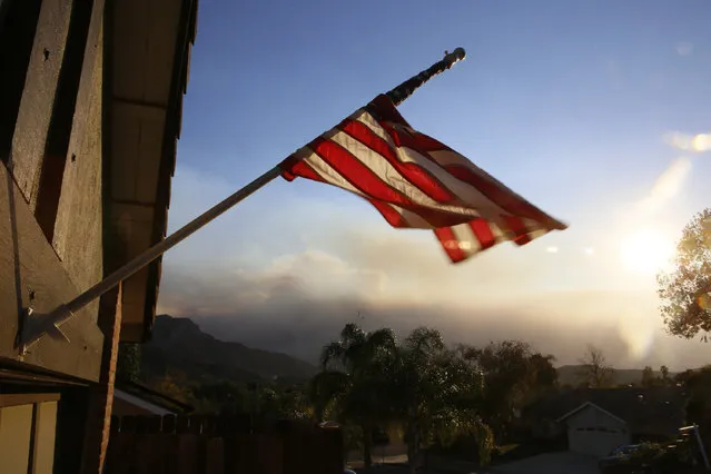 A flag is seen partially wrapped up in its pole due to heavy winds, outside the home of the ex-Marine Ian David Long, who killed 12 people at a country music bar Wednesday, in Newbury Park, Calif., Friday, November 9, 2018. Wildfire smoke fills the sky in the background. (Photo by Damian Dovarganes/AP Photo)