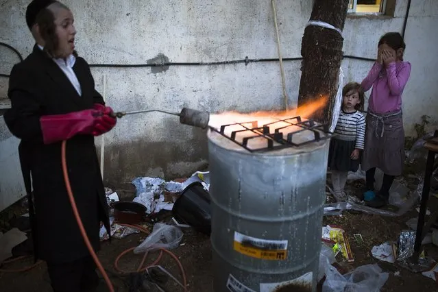 An ultra-Orthodox Jewish boy heats part of gas burner over a fire to remove remains of leaven in preparation for the upcoming Jewish holiday of Passover in the city of Ashdod April 2, 2015. Passover, which starts on Friday, commemorates the flight of Jews from ancient Egypt, as described in the Exodus chapter of the Bible. According to the account, the Jews did not have time to prepare leavened bread before fleeing to the promised land. (Photo by Amir Cohen/Reuters)