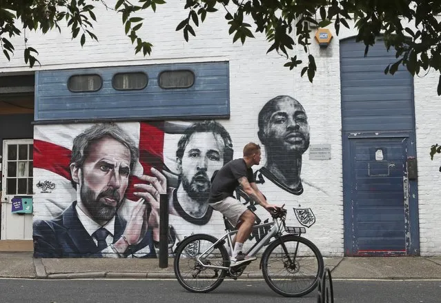 A man cycles past a mural depicting England's manager Gareth Southgate, captain Harry Kane and Raheem Sterling, from left, painted on a wall near Vinegar Yard in south London, Wednesday July 14, 2021. England lost the Euro 2020 soccer championship final match to Italy on Sunday July 11. (Photo by Tony Hicks/AP Photo)