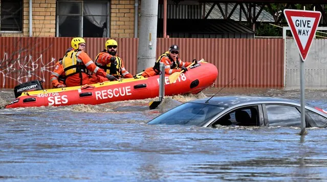 Emergency workers look at a submerged car on a flooded street in the Melbourne suburb of Maribyrnong on October 14, 2022. (Photo by William West/AFP Photo)