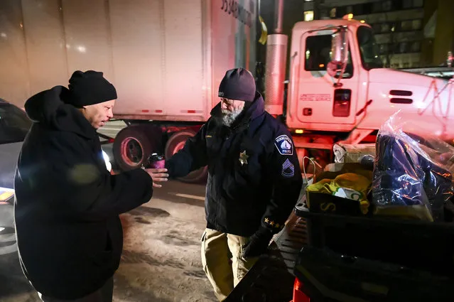 Minneapolis Police Sgt. Grant Snyder, right, hands a cup of hot chocolate to Dawone Boclair outside the public library on Hennepin Avenue in downtown Minneapolis, as the temperatures dipped well below freezing, Tuesday, January 29, 2019. Snyder will be hitting the streets Tuesday and Wednesday night during the height of the big chill to check on the welfare of homeless people who haven't made it into a shelter. (Photo by Aaron Lavinsky/Star Tribune via AP Photo)