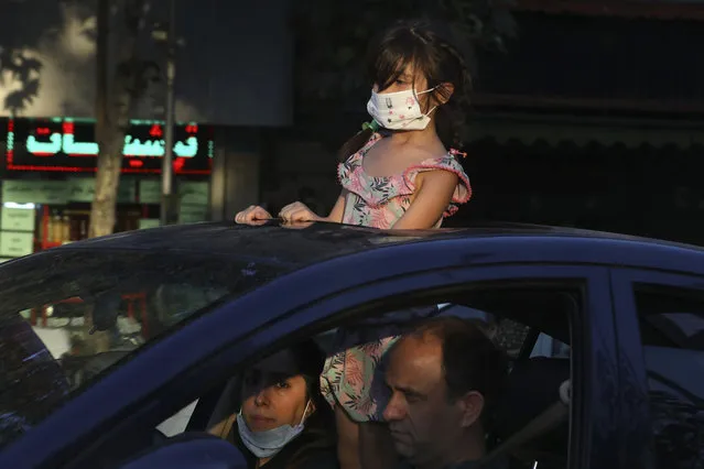 A girl wearing a protective face mask to help prevent the spread of the coronavirus looks through the sunroof of her family car on a street in central Tehran, Iran, Sunday, August 8, 2021. (Photo by Vahid Salemi/AP Photo)