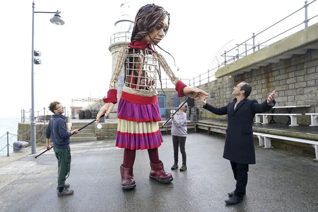 Actor Jude Law, right, looks at Little Amal, a 3.5-meter-tall puppet of a nine-year-old Syrian girl, as it arrives at Folkestone Beach, Kent, Tuesday, October 19, 2021 as part of the Handspring Puppet Company's “The Walk”. The puppet started her journey in Turkey on 27 July and has travelled nearly 8,000 km across Greece, Italy, Germany, Switzerland, Belgium and France, symbolizing millions of displaced children. (Photo by Gareth Fuller/PA Wire via AP Photo)
