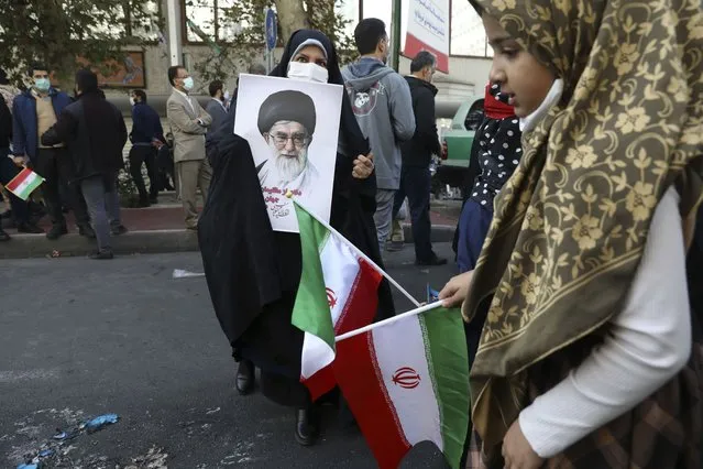 A demonstrator holds a portrait of the Iranian Supreme Leader Ayatollah Ali Khamenei as a girl holds the country's national flag in a rally in front of the former U.S. Embassy commemorating the anniversary of its 1979 seizure in Tehran, Iran, Thursday, November 4, 2021. The embassy takeover triggered a 444-day hostage crisis and break in diplomatic relations that continues to this day. (Photo by Vahid Salemi/AP Photo)