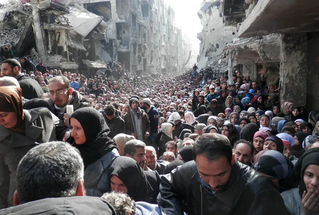 A handout picture released by the United Nation Relief and Works Agency (UNRWA) on February 26, 2014 shows residents of Syria's besieged Yarmuk Palestinian refugee camp, south of Damascus, crowding a destroyed street during a food distribution led the UN agency, on January 31, 2014. (Photo by AFP Photo/UNRWA)