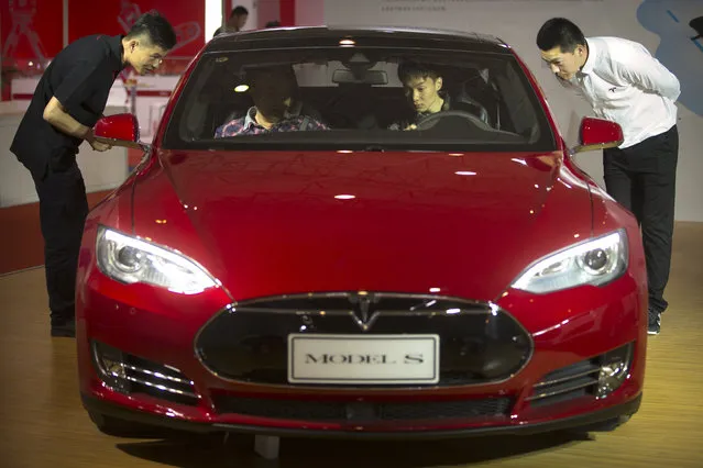 Staff members talk with visitors as they sit inside a Tesla Model S electric car on display at the Beijing International Automotive Exhibition in Beijing, Monday, April 25, 2016. (Photo by Mark Schiefelbein/AP Photo)
