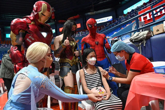 Performers dressed as superhero characters pose with a child receiving the Pfizer-BioNtech Covid-19 vaccine for children aged 5-11 at a gym in San Juan City, suburban Manila on February 7, 2022. (Photo by Ted Aljibe/AFP Photo)