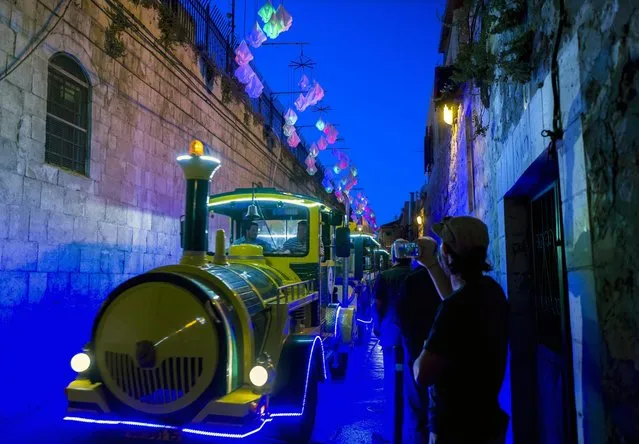 The illuminated installation “Colored Origami” hangs in the Armenian Quarter of Jerusalem's Old City as a tourist train carries people toward the Western Wall area and the Jewish Quarter, during the Festival of Light in Jerusalem, Israel, 25 May 2016. The exhibit is from Italy and produced by Gloria Ranchi and Claudio Benghi. The event runs from 25 May to 02 June. (Photo by Jim Hollander/EPA)