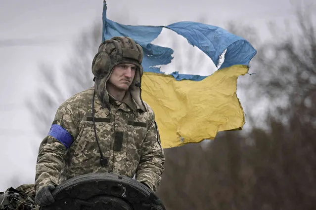 A Ukrainian serviceman is backdropped by his country's flag while standing on a tank, outside Kyiv, Ukraine, Saturday, April 2, 2022. As Russian forces pull back from Ukraine's capital region, retreating troops are creating a “catastrophic” situation for civilians by leaving mines around homes, abandoned equipment and “even the bodies of those killed”, President Volodymyr Zelenskyy warned Saturday. (Photo by Vadim Ghirda/AP Photo)