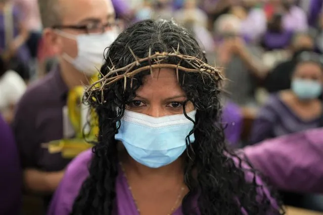 A devotee of a statue of Jesus carrying a cross known as the Nazareno de San Pablo, wearing a crown of thorns and the color purple, prays inside the Basilica of St. Teresa during Holy Week celebrations, in Caracas, Venezuela, Wednesday, April 13, 2022. After two years of COVID-19 restrictions the doors of the famous church opened its doors on Wednesday where the venerated statue resides. (Photo by Ariana Cubillos/AP Photo)