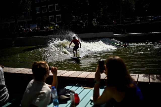 People watch a surfer riding on a canal while having a drink on a terrasse in Rotterdam on August 11, 2024. (Photo by Julien de Rosa/AFP Photo)