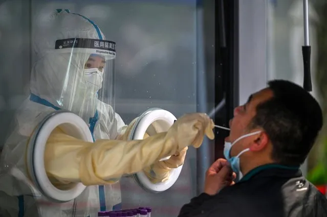 A health worker takes a swab sample from a man during a Covid-19 coronavirus lockdown in the Jing'an district in Shanghai on May 27, 2022. (Photo by Hector Retamal/AFP Photo)