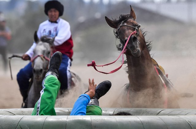 A horse rider of team Uzbekistan (Bottom) falls as a rider of team Russia (Red) looks on (L) during the traditional Central Asian sport of Kok-Boru (Gray Wolf) or Buzkashi (Goat Grabbing) in the Kok-Boru World Cup in Cholpon-Ata near Issyk-Kule lake, some 250kms east of Bishkek, on August 14, 2023. Mounted players compete for points by throwing a stuffed sheepskin into a well. (Photo by Vyacheslav Oseledko/AFP Photo)