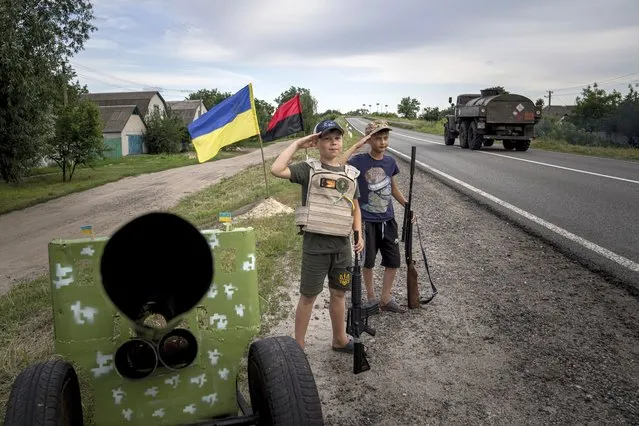 Maksym and Andrii 11, years old boys, salute to Ukrainian soldiers holding plastic guns as they play at the self-made checkpoint on the highway in Kharkiv region, Ukraine, Wednesday, July 20, 2022. (Photo by Evgeniy Maloletka/AP Photo)