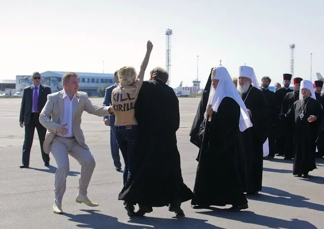 A topless protester from the Ukrainian feminist group Femen is blocked by a security guard and a priest as she tries to throw herself at the leader of the Russian Orthodox Church