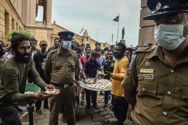 Sweets are offered to military personnel as people in Colombo, Sri Lanka, celebrate on Friday, July 15, 2022, the resignation of President Gotabaya Rajapaksa the day before. Rajapaksa had fled his country early Wednesday after months of fervent protests. (Photo by Atul Loke/The New York Times)