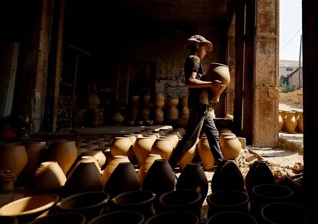 A Palestinian carries pottery in a workshop in Hebron, in the Israeli-occupied West Bank on August 4, 2022. (Photo by Mussa Qawasma/Reuters)