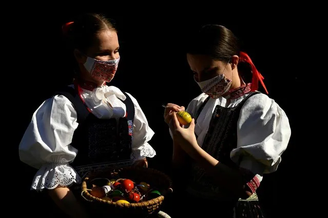 Vanda Mrazikova and Martina Kacenova, dressed in traditional costumes and protective face masks, decorate colored Easter eggs, amid the coronavirus disease (COVID-19) outbreak, in the village of Soblahov, Slovakia, April 7, 2020. (Photo by Radovan Stoklasa/Reuters)