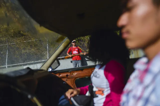 A couple drives past a member of the pro-government militias taking part in a foreign invasion drill in Caracas, Venezuela, Saturday, February 15, 2020. (Photo by Matias Delacroix/AP Photo)
