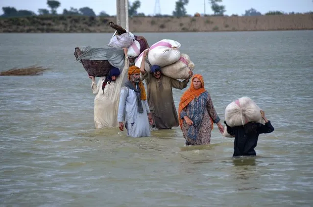 A displaced family wades through a flooded area after heavy rainfall, in Jaffarabad, a district of Pakistan's southwestern Baluchistan province, Wednesday, August 24, 2022. Rains have triggered flash floods and wreaked havoc across much of Pakistan since mid-June, leaving 903 dead and about 50,000 people homeless, the country's disaster agency said Wednesday. (Photo by Zahid Hussain/AP Photo)