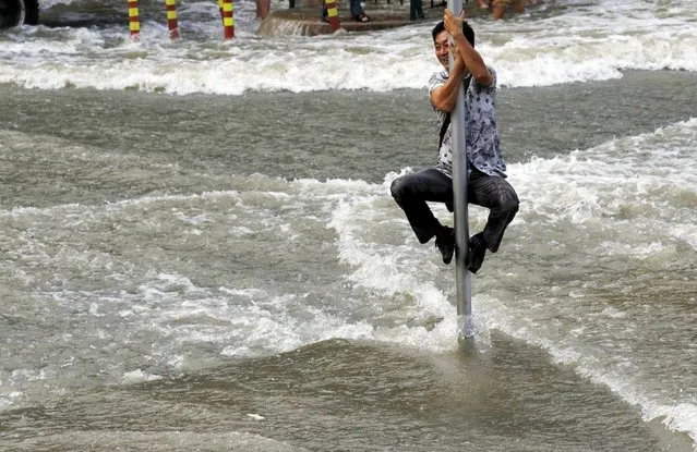 A man climbs on a road sign pole to escape the water from a tidal bore which surged past a barrier on the banks of Qiantang River, in Hangzhou, Zhejiang province, China, September 1, 2015. (Photo by Reuters/Stringer)