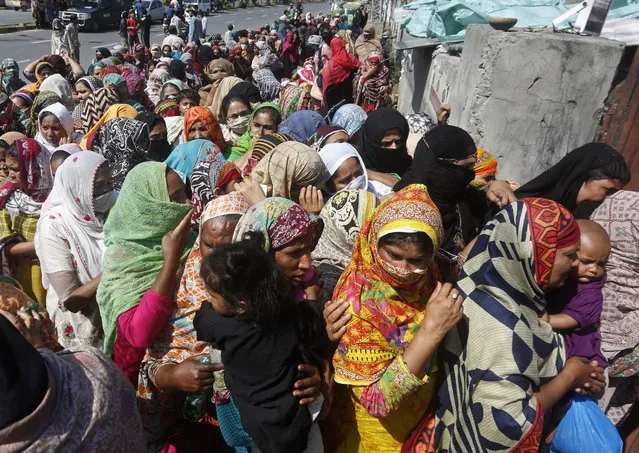 People wait to receive food assistance ahead of the Muslim fasting month of Ramadan, during a government-imposed nationwide lockdown to help contain the spread of the coronavirus, in Lahore, Pakistan, Thursday, April 23, 2020. Ramadan begins with the new moon later this week as Muslims all around the world are trying to work out how to maintain the many cherished rituals of Islam's holiest month amid the coronavirus pandemic. (Photo by K.M. Chaudhary/AP Photo)