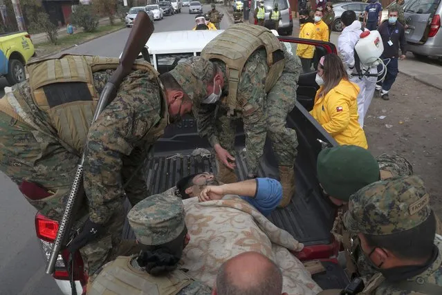 Soldiers help a city worker that fainted during an event where an army kitchen was serving food for people facing hardship because of lost income due to the new coronavirus pandemic, in Maipu, on the outskirts of Santiago, Chile, Tuesday, June 16, 2020. (Photo by Esteban Felix/AP Photo)