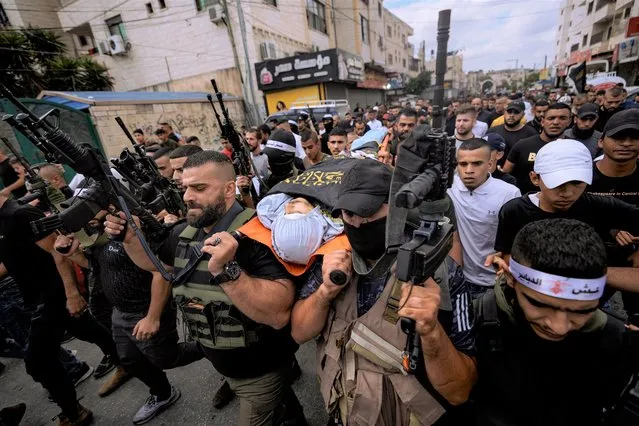 Armed Palestinians carry the body of Mahmoud Al-Sous, covered with a flag of the Islamic Jihad militant group during his funeral in the West Bank town of Jenin, Saturday, October 8, 2022. Israeli soldiers shot and killed two Palestinians on Saturday in an exchange of fire that erupted during a military raid in the West Bank. The Israeli military said it had arrested a 25-year-old operative from the Islamic Jihad militant group who has previously been imprisoned by Israel. It said the man had recently been involved in shooting attacks on Israeli soldiers. (Photo by Majdi Mohammed/AP Photo)