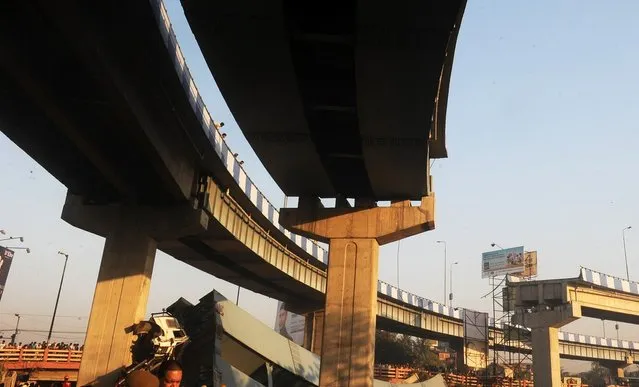 Indian onlookers stand near the collapsed portion of a flyover in Kolkata on March 3, 2013. A huge portion of a flyover on the eastern side of the Indian metropolis collapsed leaving three persons injured, the flyover connects the airport with Eastern Metropolitan Bypass and the eastern and southern suburbs.   As the debris fell into a canal running below the flyover, it took down a truck the driver and two others were rescued from the canal by fire-brigade personnel and locals. (Photo by Dibyangshu Sarkar/AFP Photo)