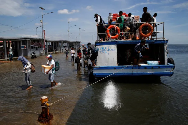 Passengers of a boat walk through rising sea water during high tide at Kali Adem port in Jakarta, Indonesia, January 4, 2018. (Photo by Reuters/Beawiharta)