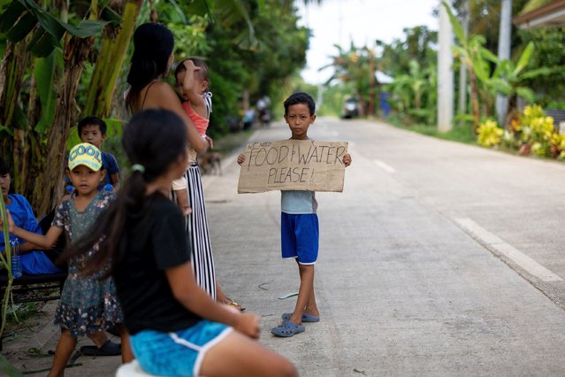 A boy holds a sign that reads “we need food and water please” as he stands by on the roadside with other residents waiting for relief goods, days after the magnitude 6.9 quake in Daanbantayan, Cebu, Philippines, on October 3, 2025. (Photo by Eloisa Lopez/Reuters)