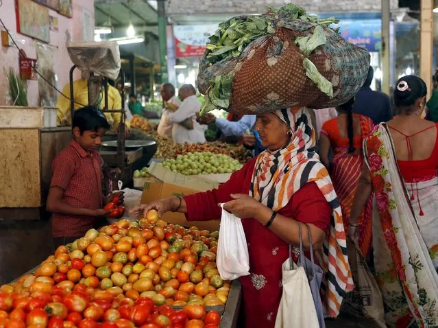 A woman carrying cabbage leaves on her head buys tomato at a market in Ahmedabad, India, November 9, 2015. (Photo by Amit Dave/Reuters)