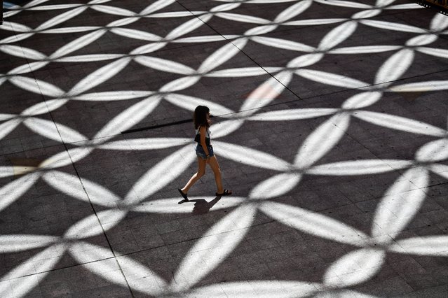 Sun shades form a pattern in a square near a shopping center as a woman walks by during high temperatures in Seville on July 8, 2025 (Photo by Cristina Quicler/AFP Photo)