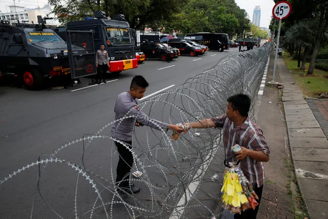 A policeman buys a snack as he stands guard in front of U.S. embassy in Jakarta, Indonesia, during Indonesia Muslim rally to support Palestinians and against the U.S. moving its embassy to Jerusalem, May 11, 2018. (Photo by Reuters/Beawiharta)