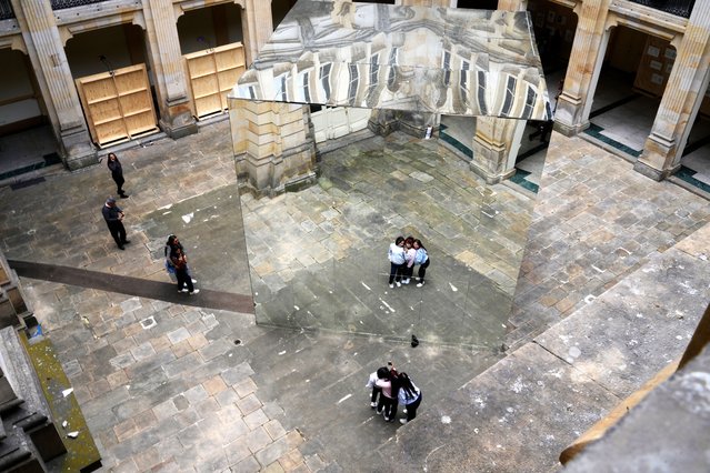 A trio poses for a photo in front of the art installation Surrender (Flag) by John Gerrard of Ireland displayed in a courtyard of the Palacio de San Francisco, as part of the first art biennial in Bogota, Colombia, Tuesday, September 23, 2025. (Photo by Fernando Vergara/AP Photo)