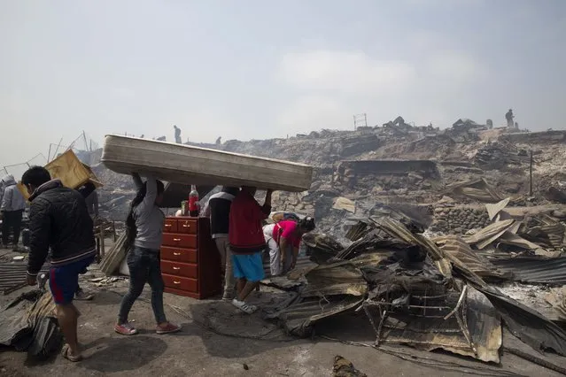 A family salvages a mattress from charred debris following an early morning fire that destroyed hundreds of homes, in the shantytown known as Cantagallo, in Lima, Peru, Friday, November 4, 2016. The huge fire destroyed hundreds of homes where more than 3,000 members of Lima’s Peruvian Amazon indigenous community have settled. It took firefighters more than six hours to get the fire under control, due to lack of water and difficult access to the area because of its narrow streets. No deaths have been reported. (Photo by Martin Mejia/AP Photo)